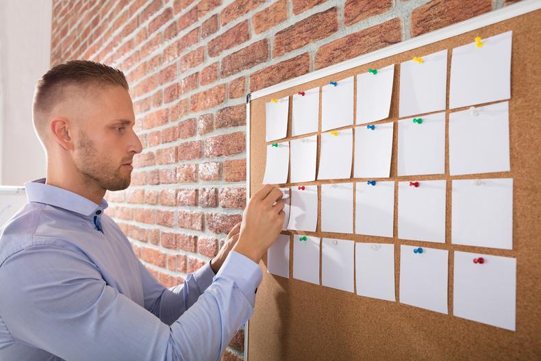 Man arranging pieces of paper on a cork board