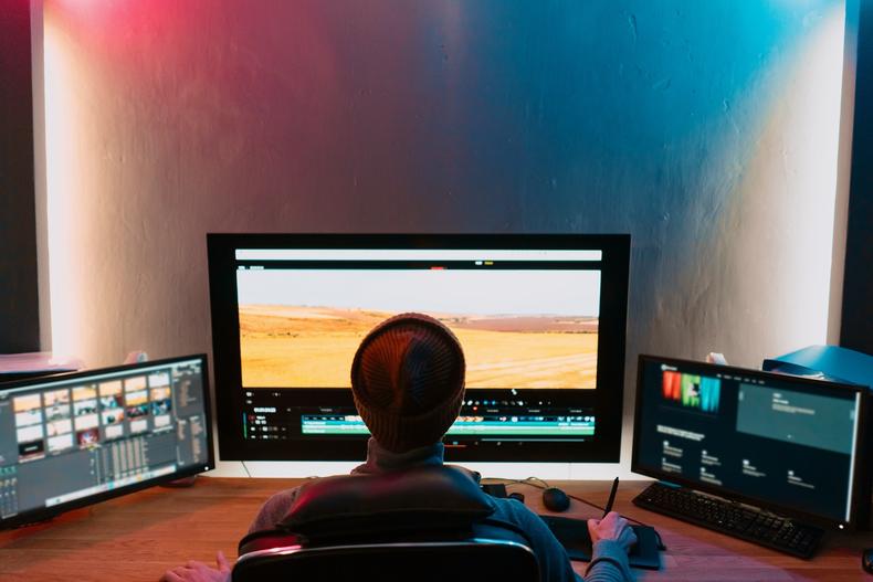 Video editor in front of three computer monitors