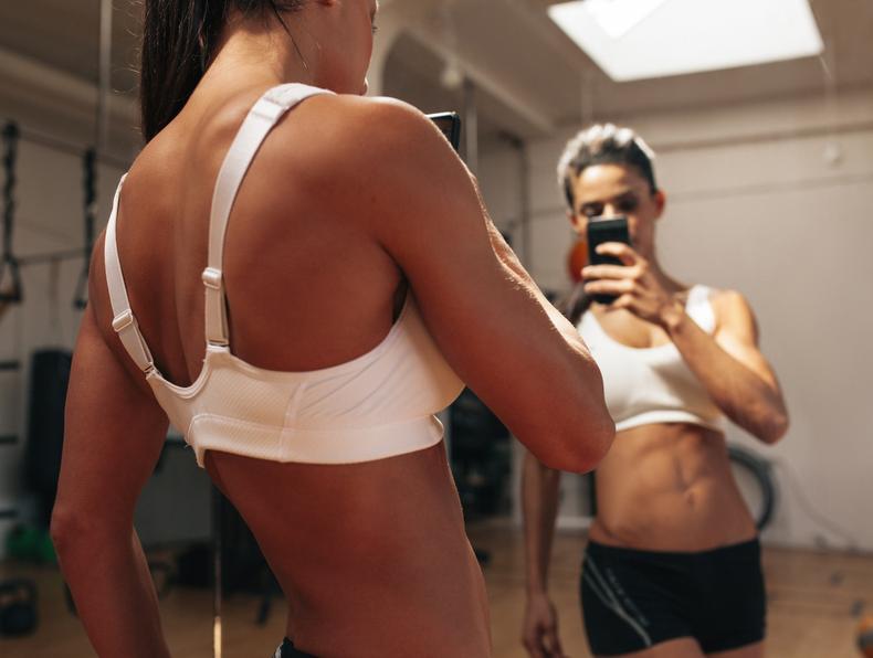 Woman taking photo of her abs in front of a mirror